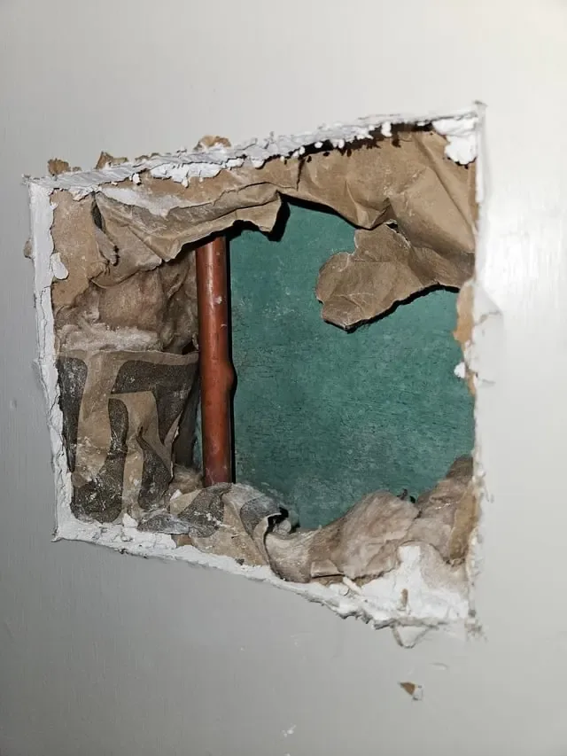 Drywall opened to reach a leaking copper water pipe inside the wall