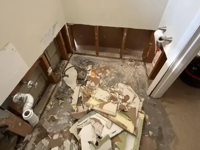 Removed wallboard collected on a floor beside exposed lower wall studs